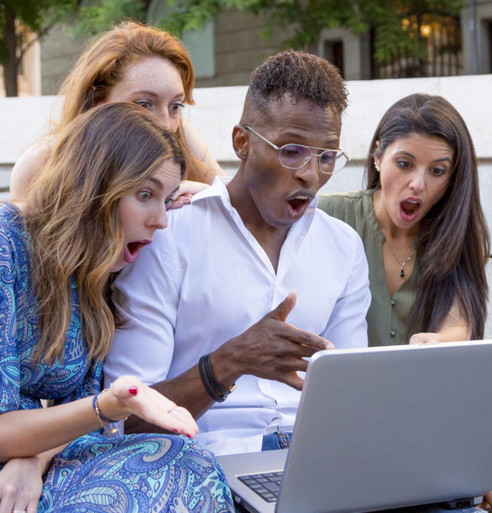 Three women and a man looking at a laptop with a surprised face in a urban park