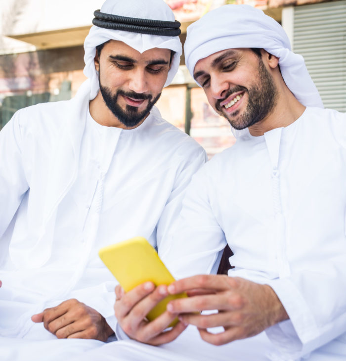 Middle-eastern young adults wearing kandora walking outdoors in Dubai - Two businessmen meeting outdoors